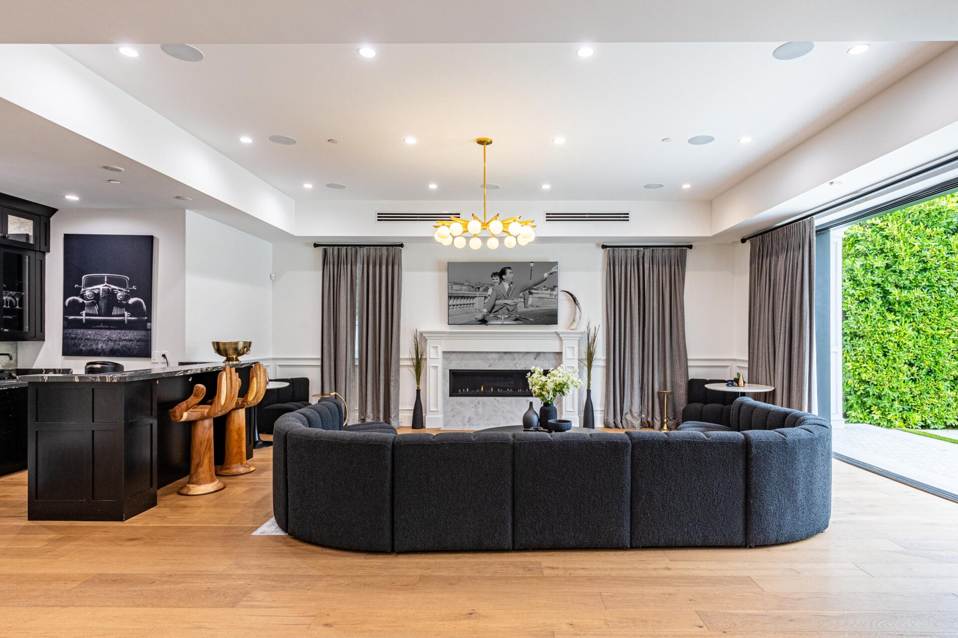A large curved black couch wraps around the middle of the room, while wide doors along the exterior wall open directly to the backyard.