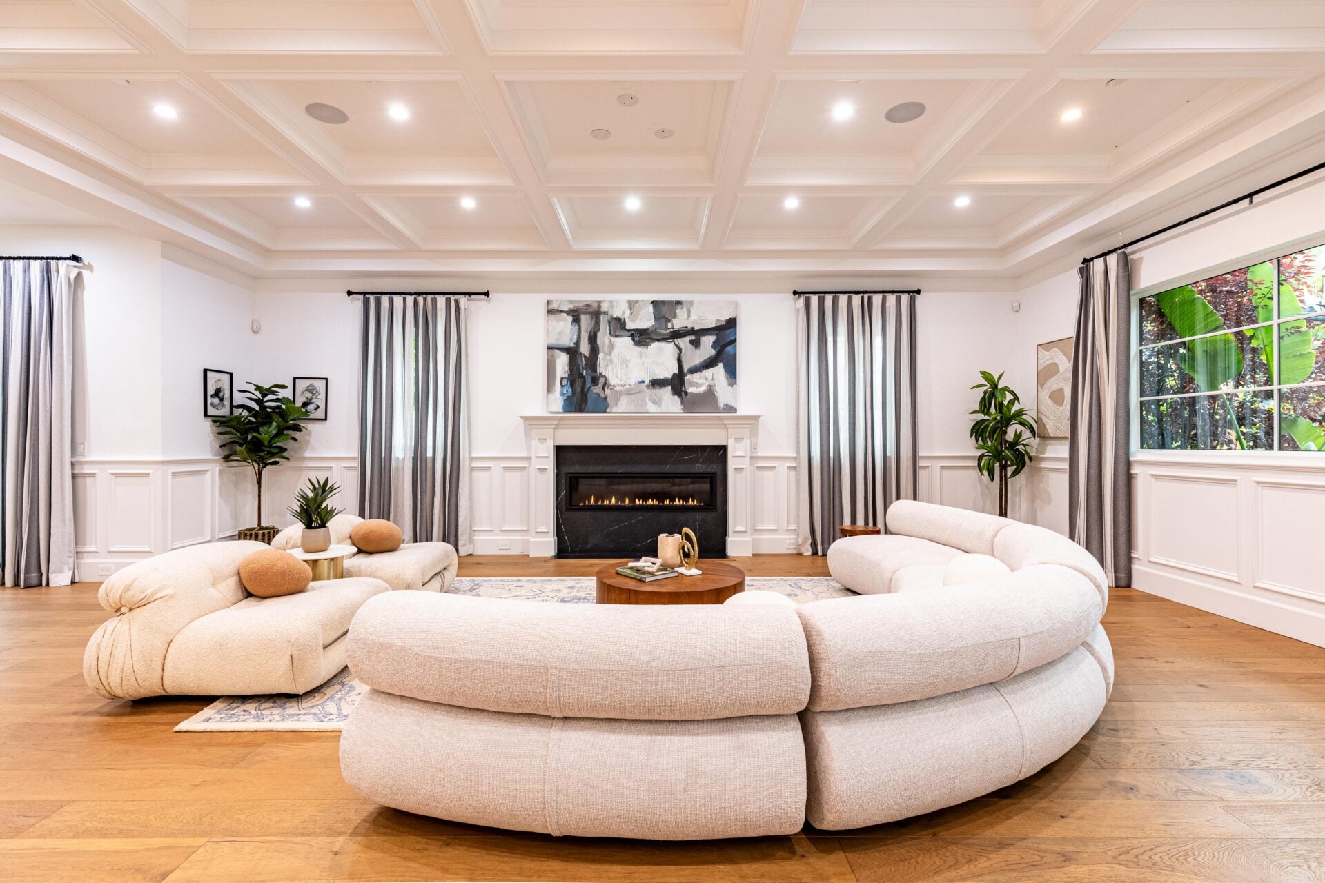 Facing the fireplace is a curved cream sofa and cushioned chairs that wrap around a round wood coffee table, 