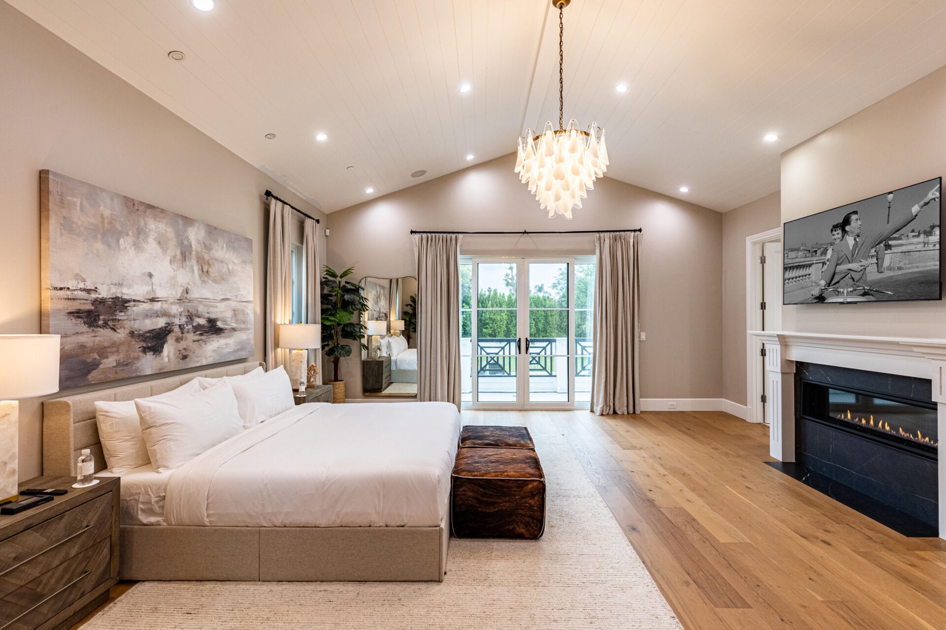 The primary bedroom opens beneath a high vaulted ceiling, with the bed set along one side of the room and a fireplace built into the opposite wall. 