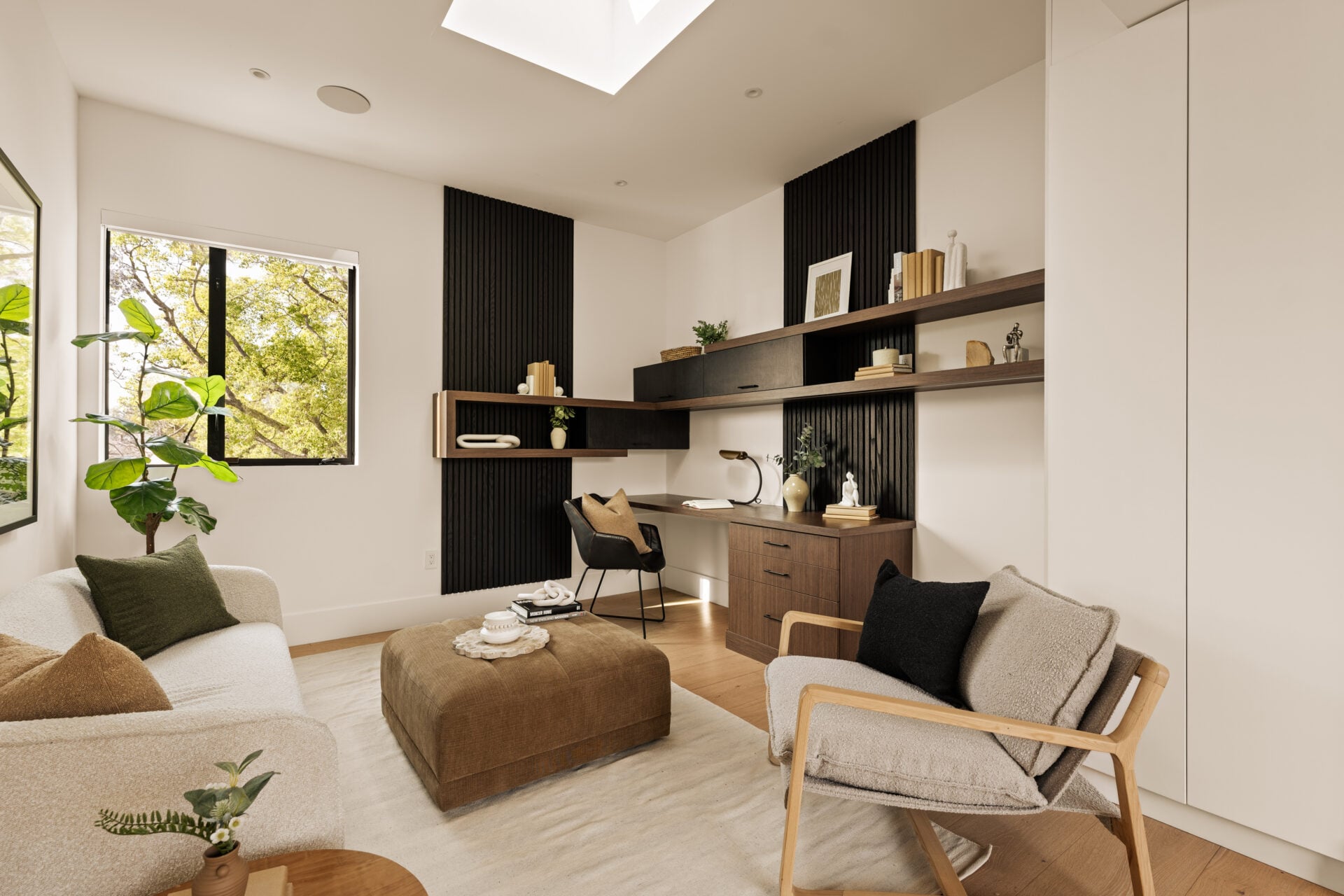 Built-in cabinetry and floating wood shelves wrap the far wall near the desk, while a small sitting area sits on the other side of the room.