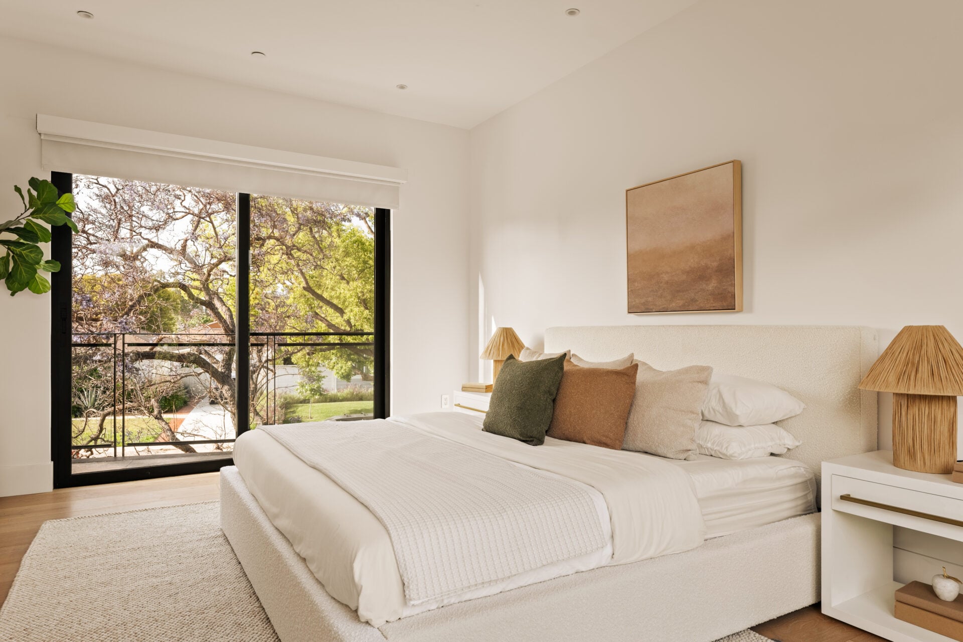 The primary bedroom is positioned along the front of the house, with the bed set opposite a wall of black-framed glass that opens directly to a private balcony.