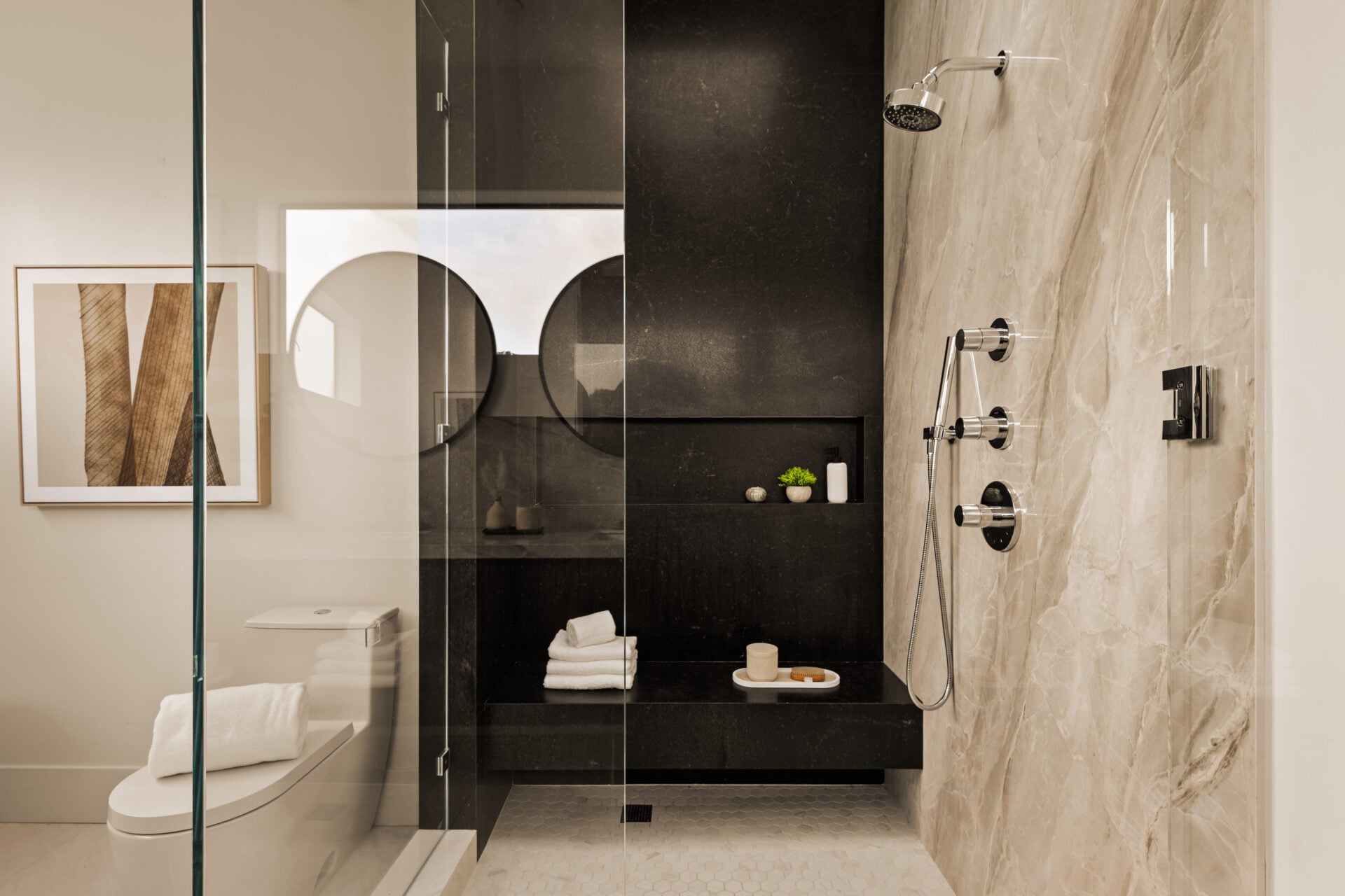 Across from the vanity is a large glass-enclosed shower lined in light stone on one side and dark stone on the other. 