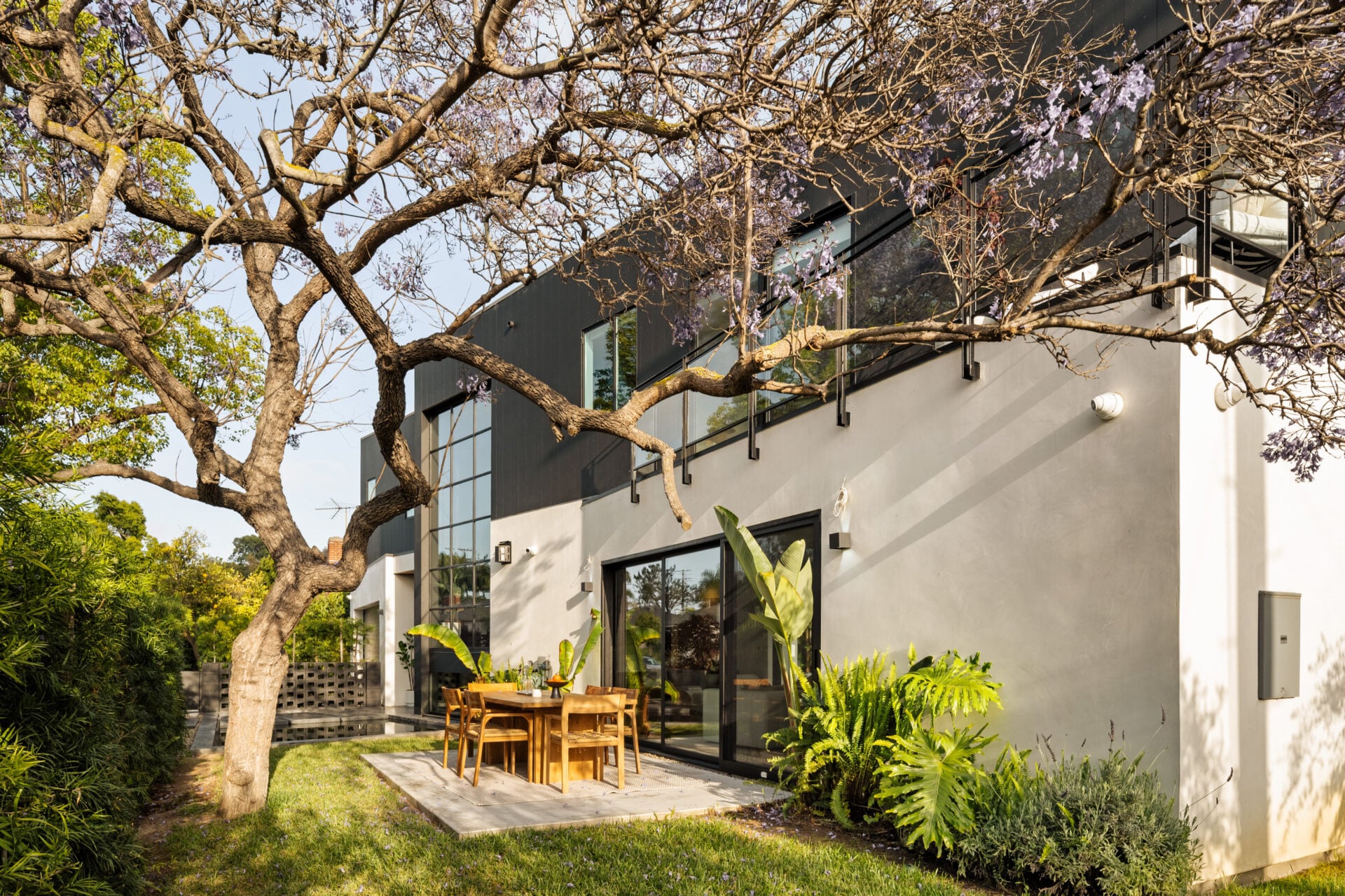 A wood dining table sits directly outside the sliding glass doors beneath a tree.