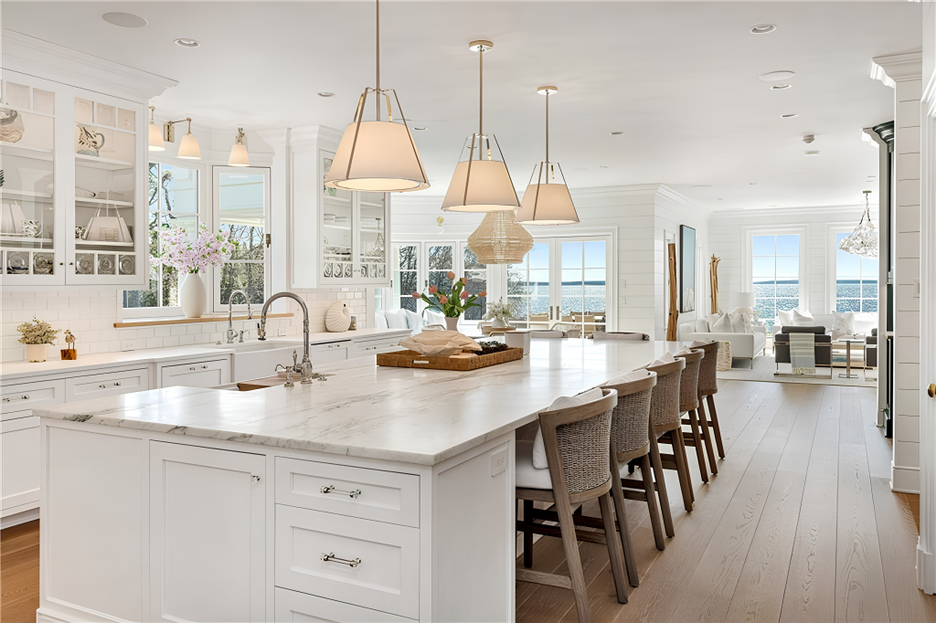 White cabinetry sits above marble countertops, while an oversized island runs through the center with seating along one side and a sink on the other.