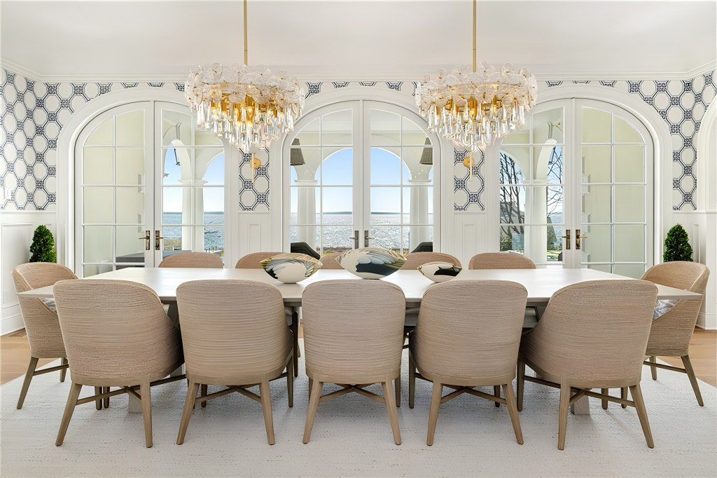 The formal dining room sits along the water-facing side of the house, with a long table centered beneath a pair of shimmering chandeliers. 