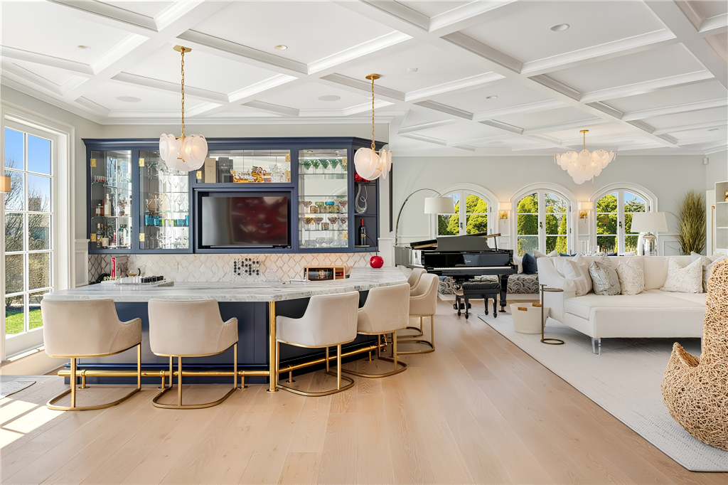 A bar stretches beneath a marble counter, with upholstered stools pulled up in front and dark cabinetry rising behind it around glass-fronted storage and a TV.