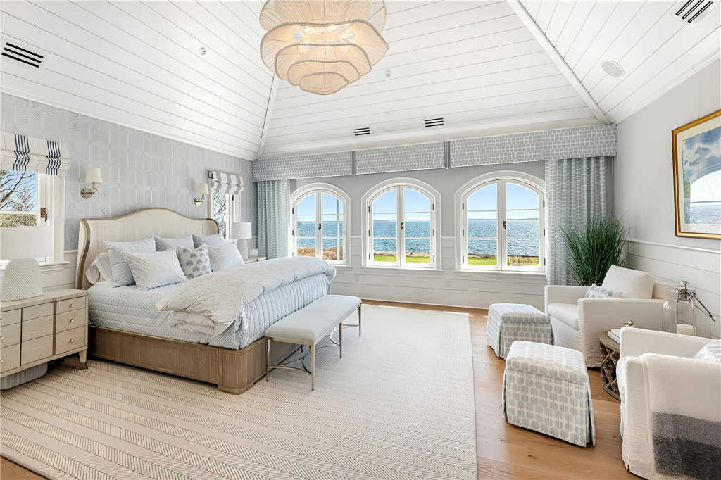 The bed sits beneath the vaulted ceiling, while a separate sitting area occupies the opposite side of the room with a pair of armchairs and ottomans.