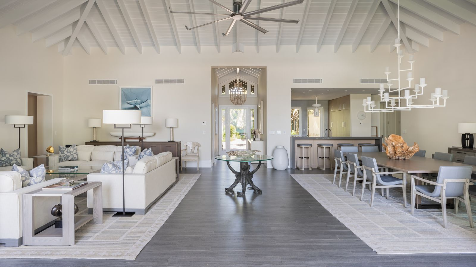 An expansive great room set across wood-look porcelain floors, with the living room, dining area, and kitchen arranged within one open space beneath a vaulted ceiling. 