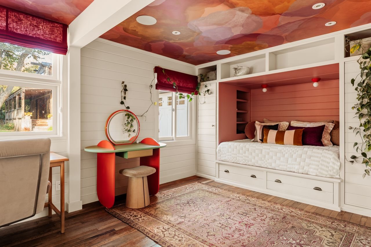 A custom vanity sits across the room between the windows, while the painted ceiling adds another layer of color overhead.