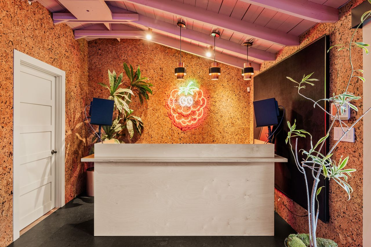 Cork walls and a raspberry neon light above a white desk.