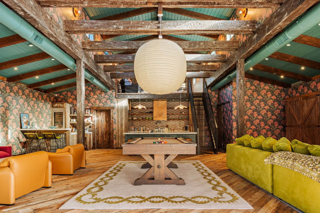 A billiards table, with multiple seating areas spread around it, including a large green couch on one side and orange leather chairs on the other. 