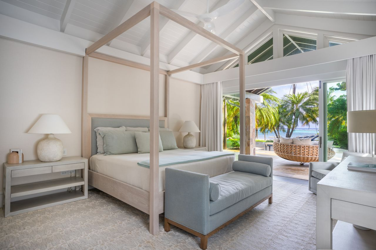 A light wood canopy bed sits beneath a vaulted ceiling and opens to a oceanfront terrace.