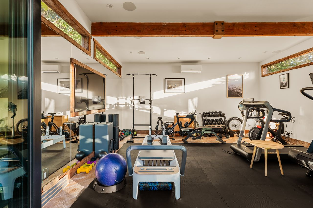 The gym includes cardio machines, free weights, strength-training equipment, and open floor space for stretching or floor work.