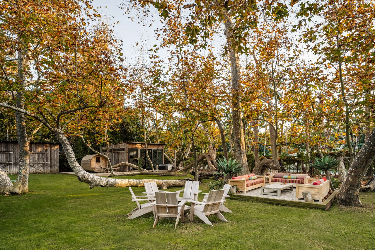 A fire pit surrounded by Adirondack chairs next to another seating area with cushioned sofas set on a gravel pad. 