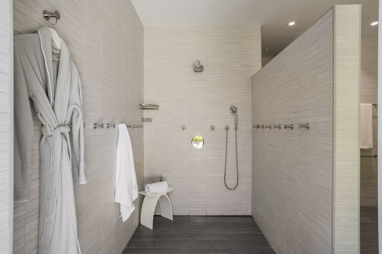 The bathroom opens into a large walk-in shower finished in the same pale tile as the surrounding walls.