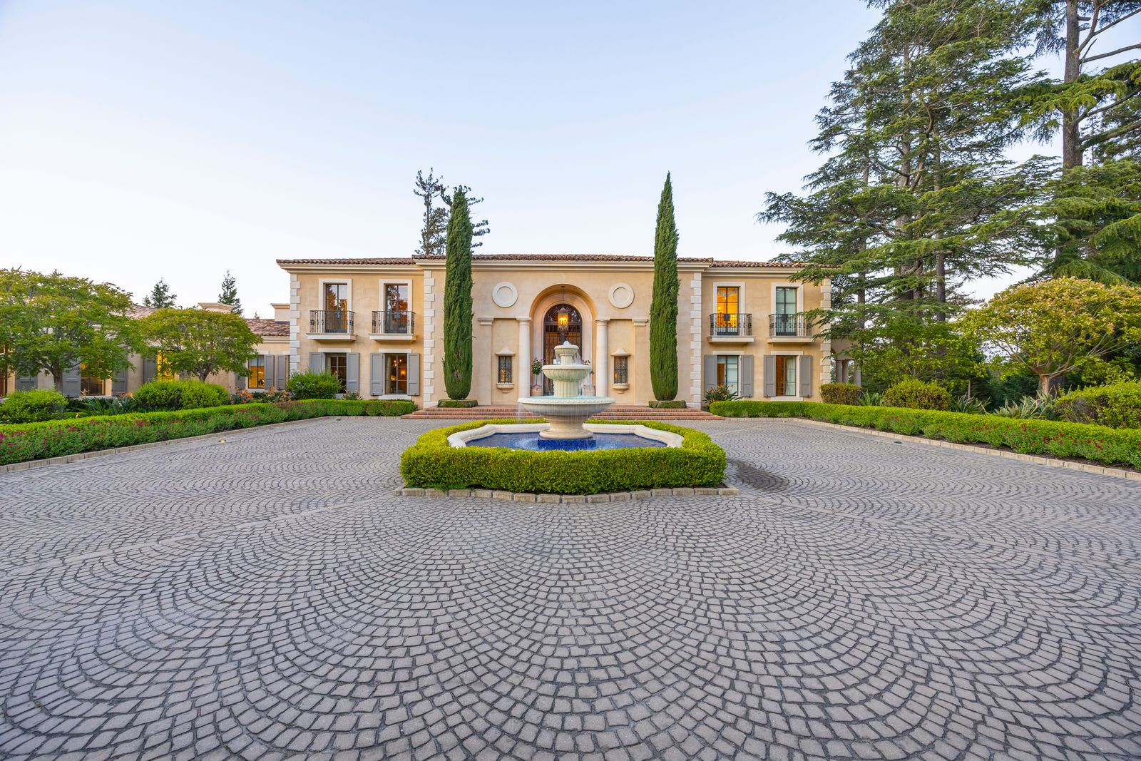 Main residence front entrance set behind a large paved driveway with a fountain in the center.