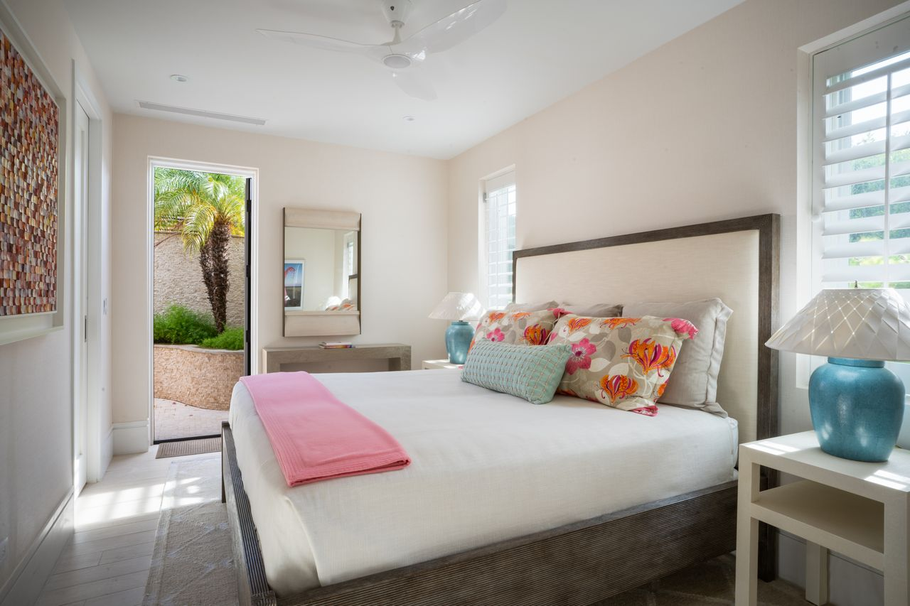 A bright bedroom with a large upholstered bed, colorful floral accents, and a door opening directly to a private garden walkway.