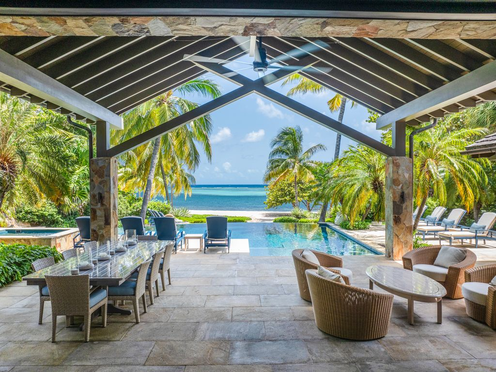 A covered terrace creates the villa’s main outdoor living and dining area with a long table on the left and a group of woven lounge chairs off to the right.