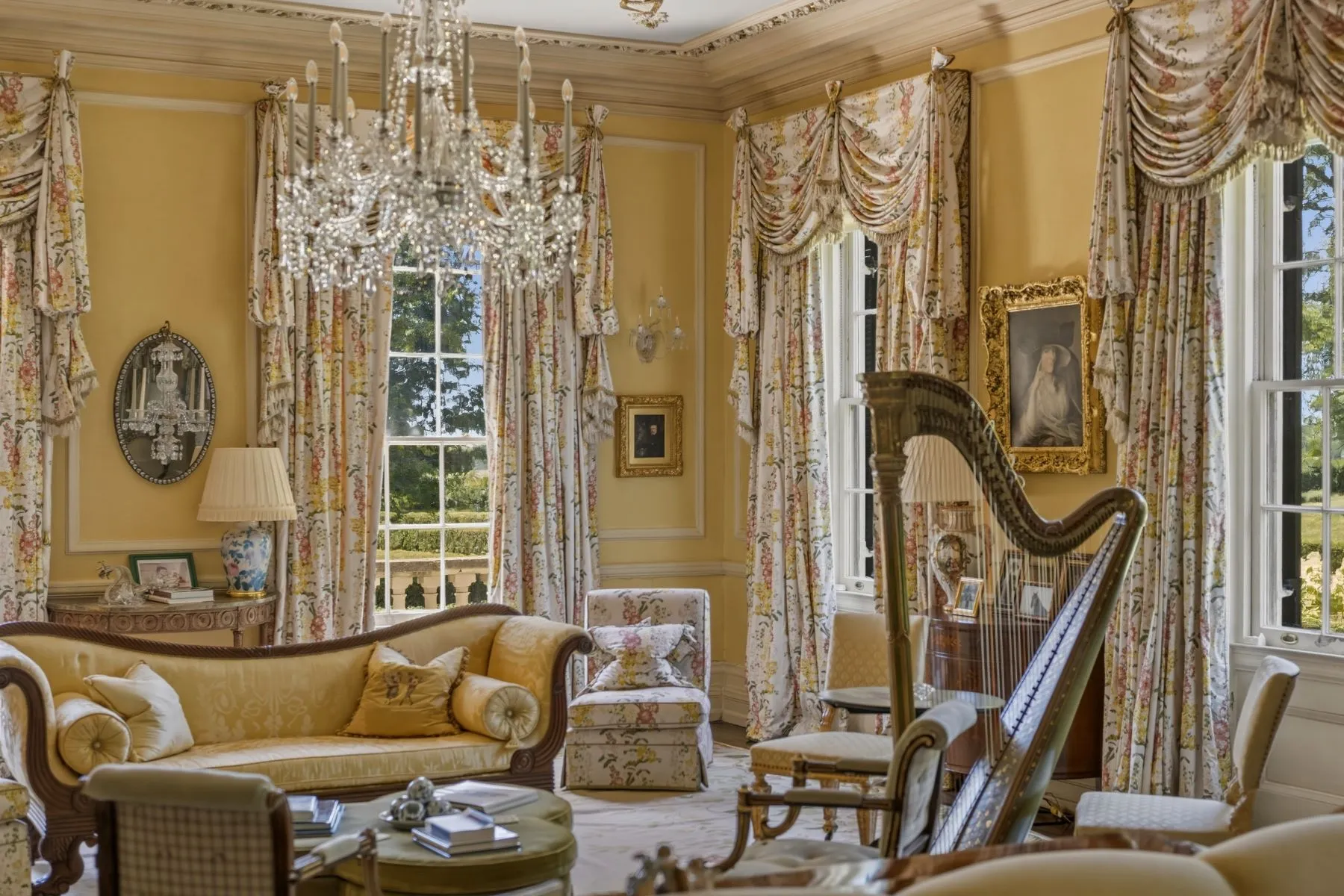 A more intimate music room features a grand harp set near windows dressed with floral drapery, bringing in garden views from several sides. 