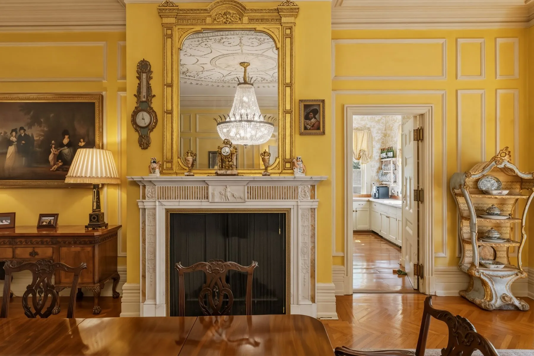 A long polished wood table sits beside the fireplace topped with an oversized mirror that reflects the sparkling chandelier.