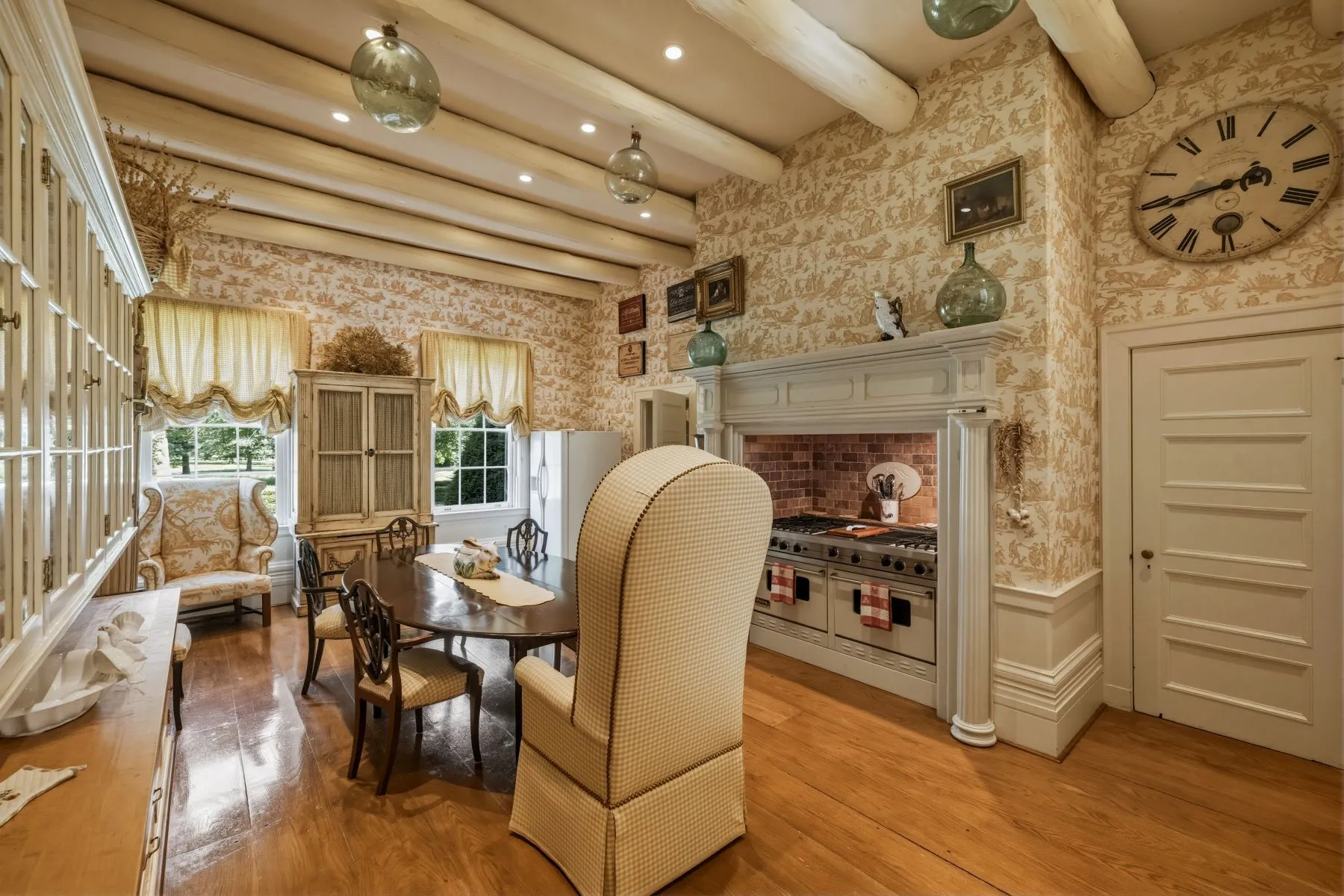 Within this room, an oval table sits in the center, while a large range with double ovens lines one side and additional cabinetry and storage is built into the opposite wall.
