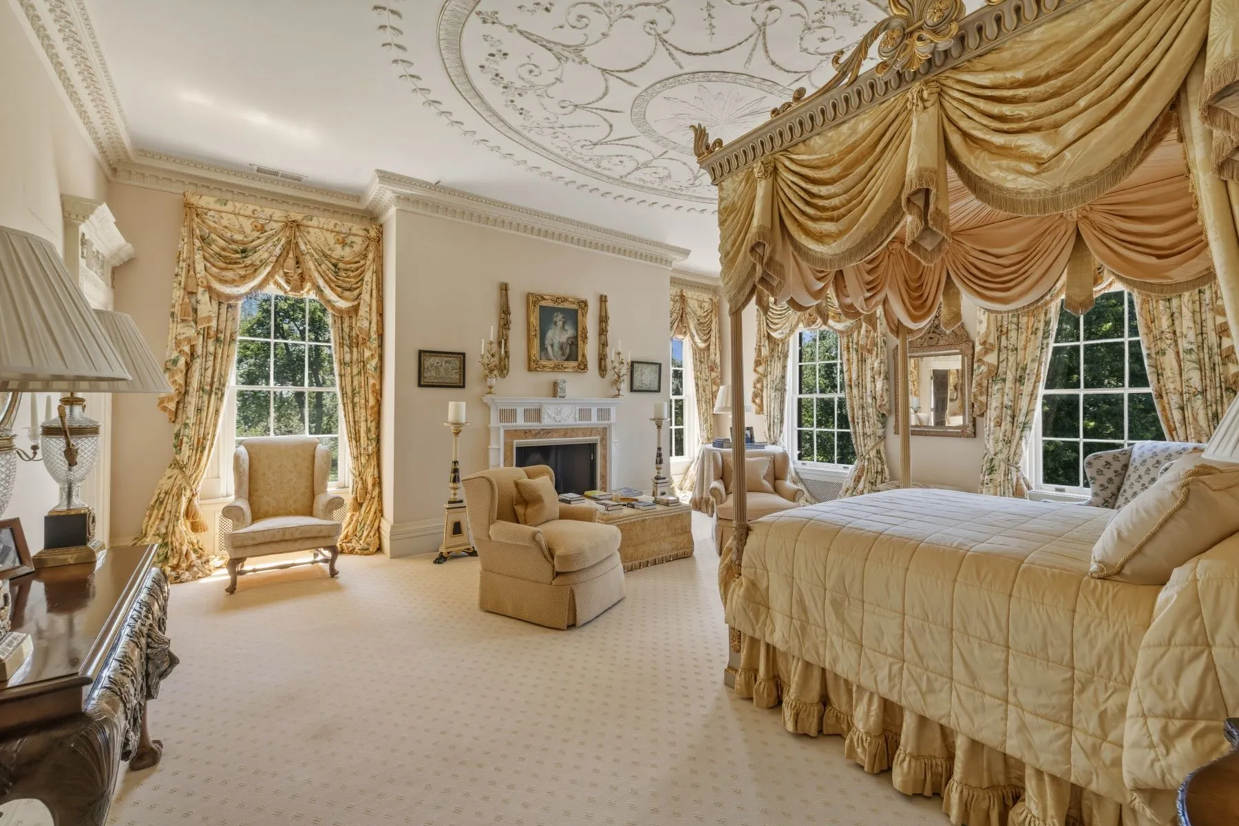 Bedroom layered in shades of gold, yellow, and pink with a canopy bed facing two armchairs that sit in front of the fireplace.