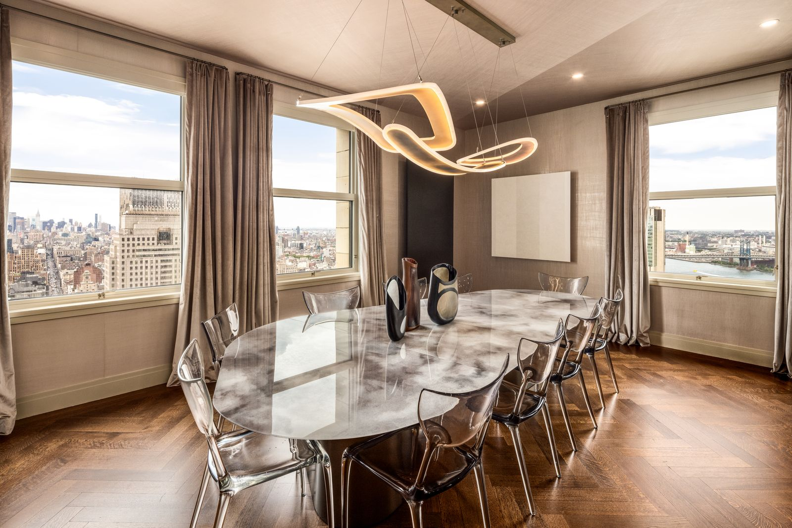 The dining area features a reflective oval table beneath a sculptural light fixture, with transparent chairs lining the edges.