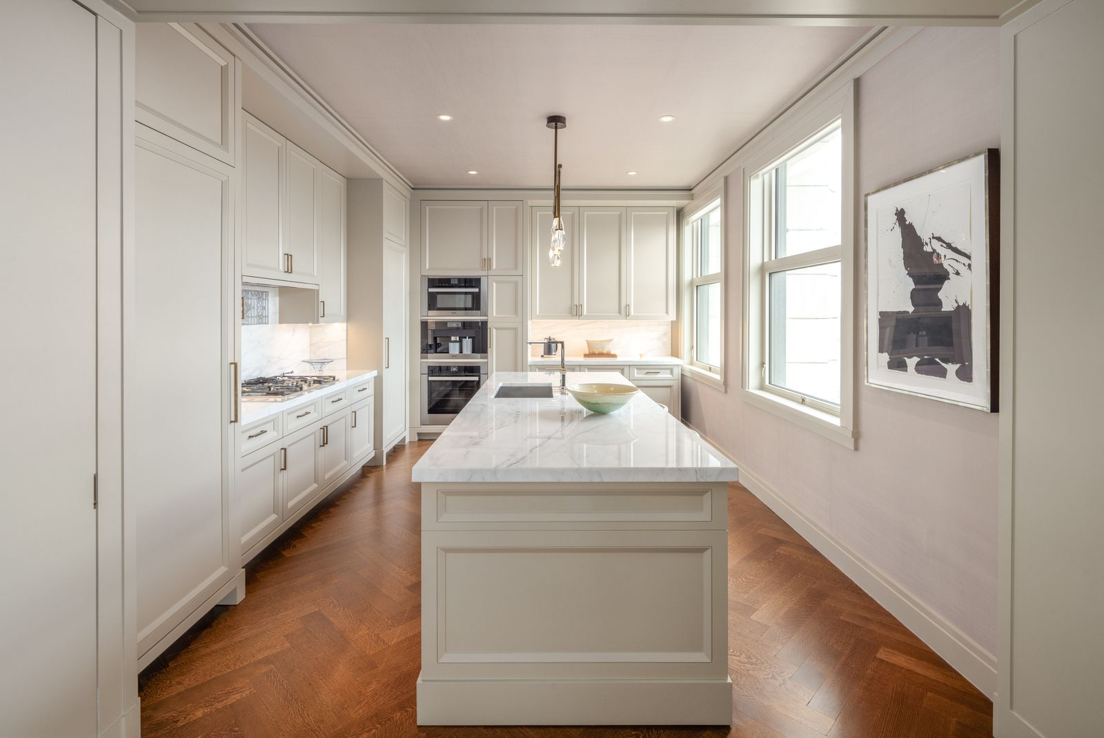 Kitchen where the oak herringbone floors continue beneath a long central island topped in Calacatta Calida marble. 