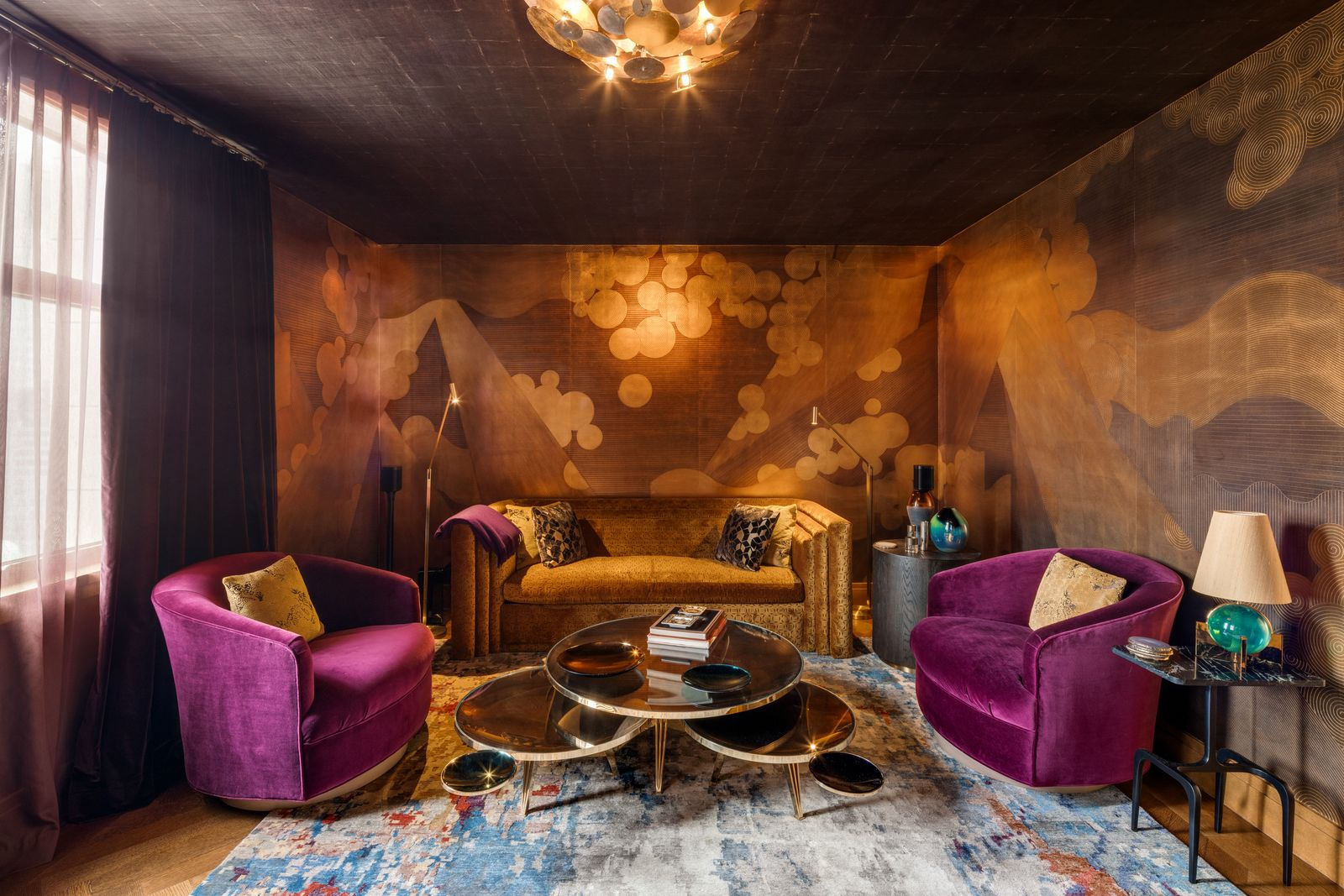 The room is furnished with a velvet sofa, a pair of purple lounge chairs, a curved chaise, and a layered coffee table in the center. 