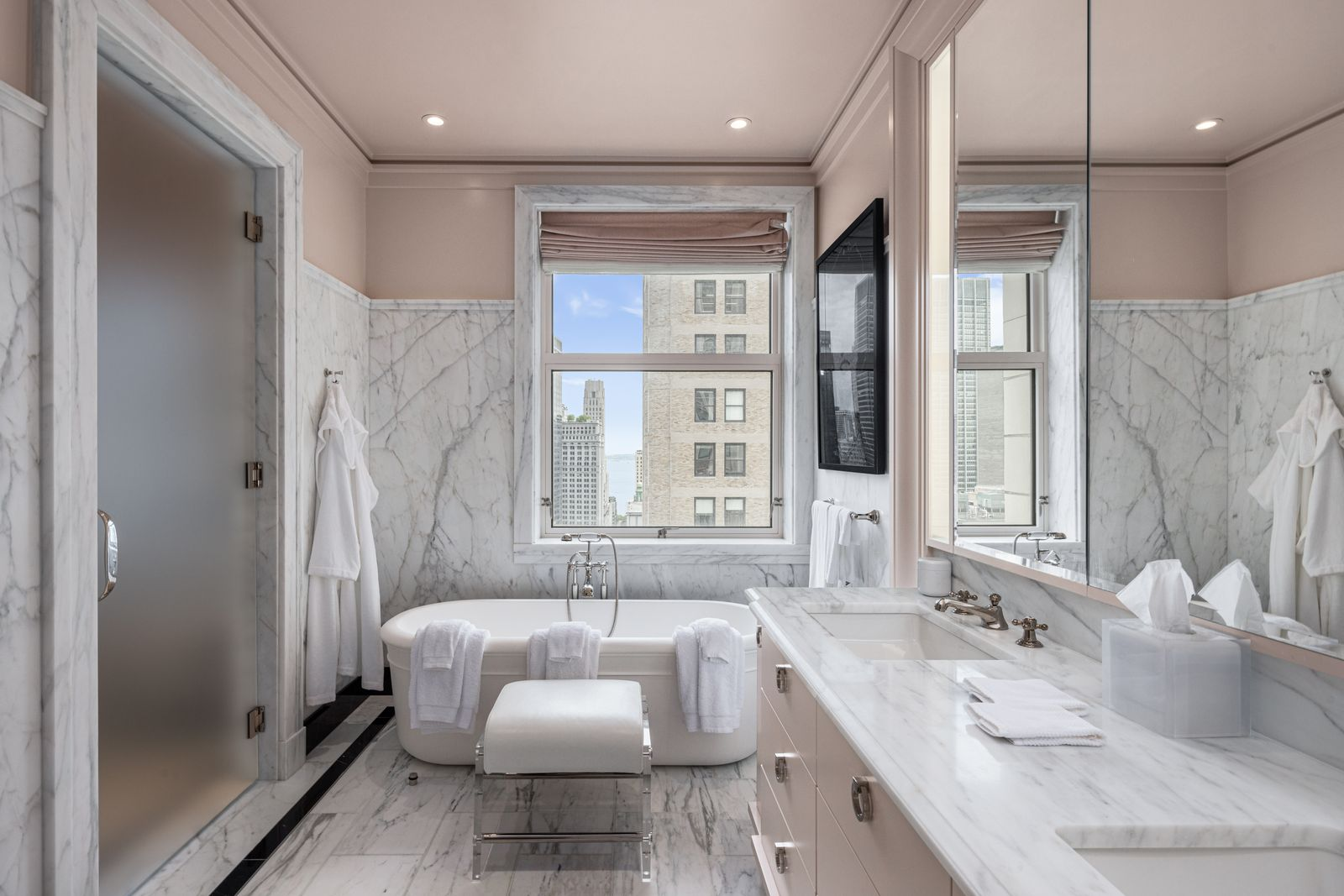 A freestanding soaking tub sits beneath the window, while the long double vanity stretches along the opposite wall beneath a wide mirror.