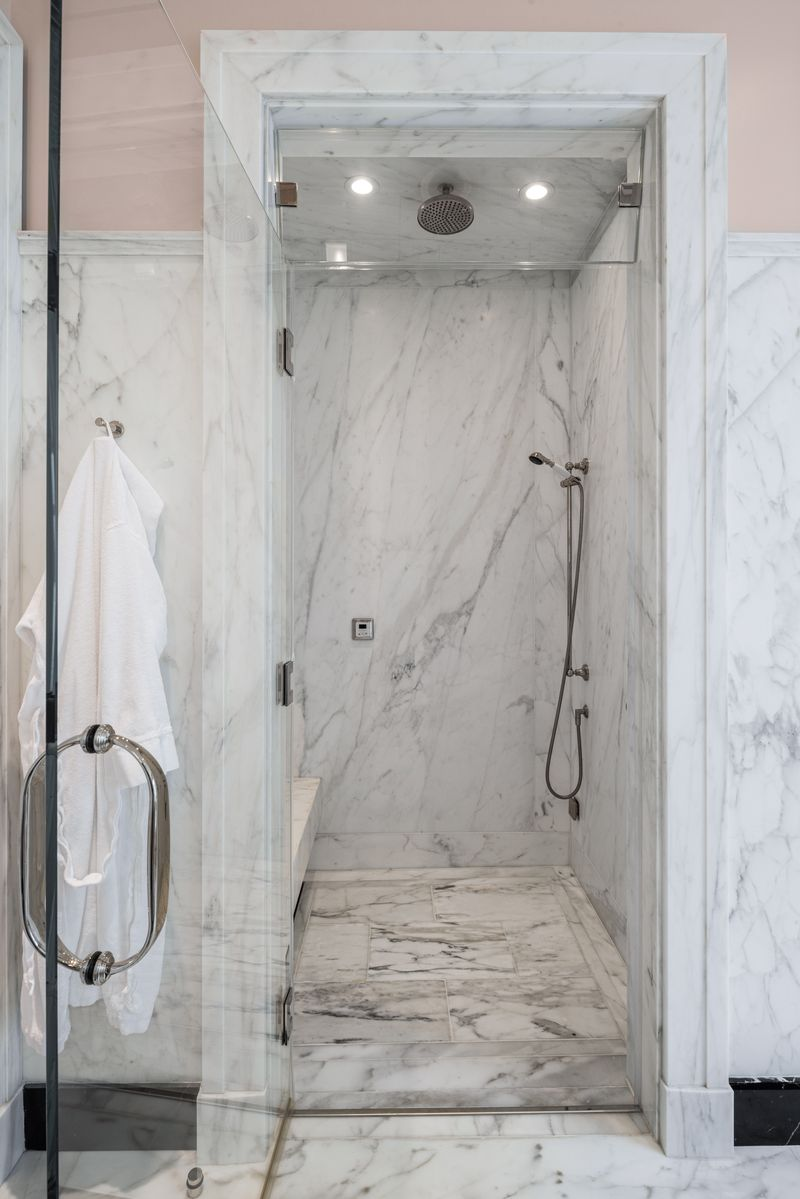Inside the steam shower, where both overhead and handheld shower fixtures are built into the marble enclosure.