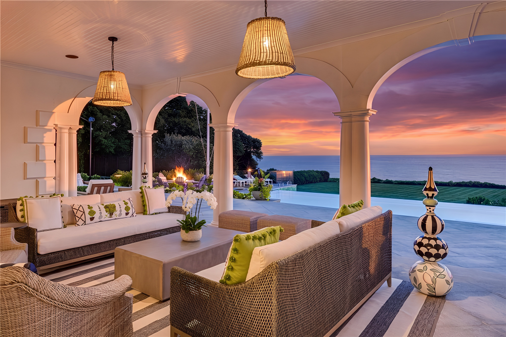 Beneath the arched covered portion, woven sofas and lounge chairs create a sheltered seating area that still opens completely toward the water.