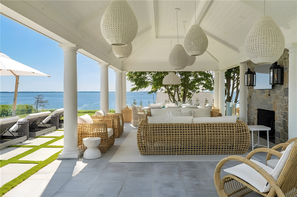 Covered loggia furnished with woven seating beneath a vaulted ceiling and includes its own fireplace and TV