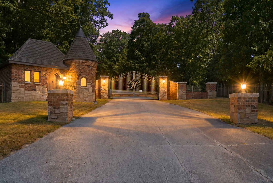 A gated entry opening onto a long driveway that winds through the wooded grounds. 