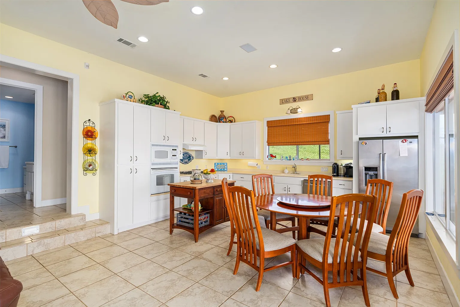 Just behind it, the kitchen is finished in white cabinetry and arranged around a compact wood island, with a round dining table placed off to the side. 