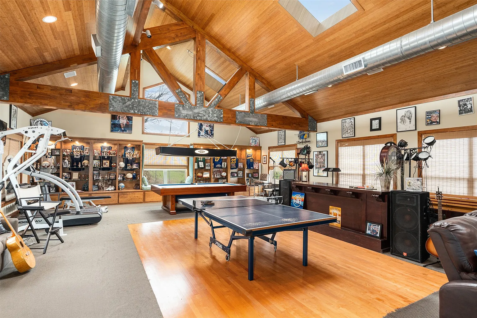 At the center, a section of wood basketball flooring doubles as a dance floor, with a ping pong table placed on top of it, and a pool table sits at the back of the room. 