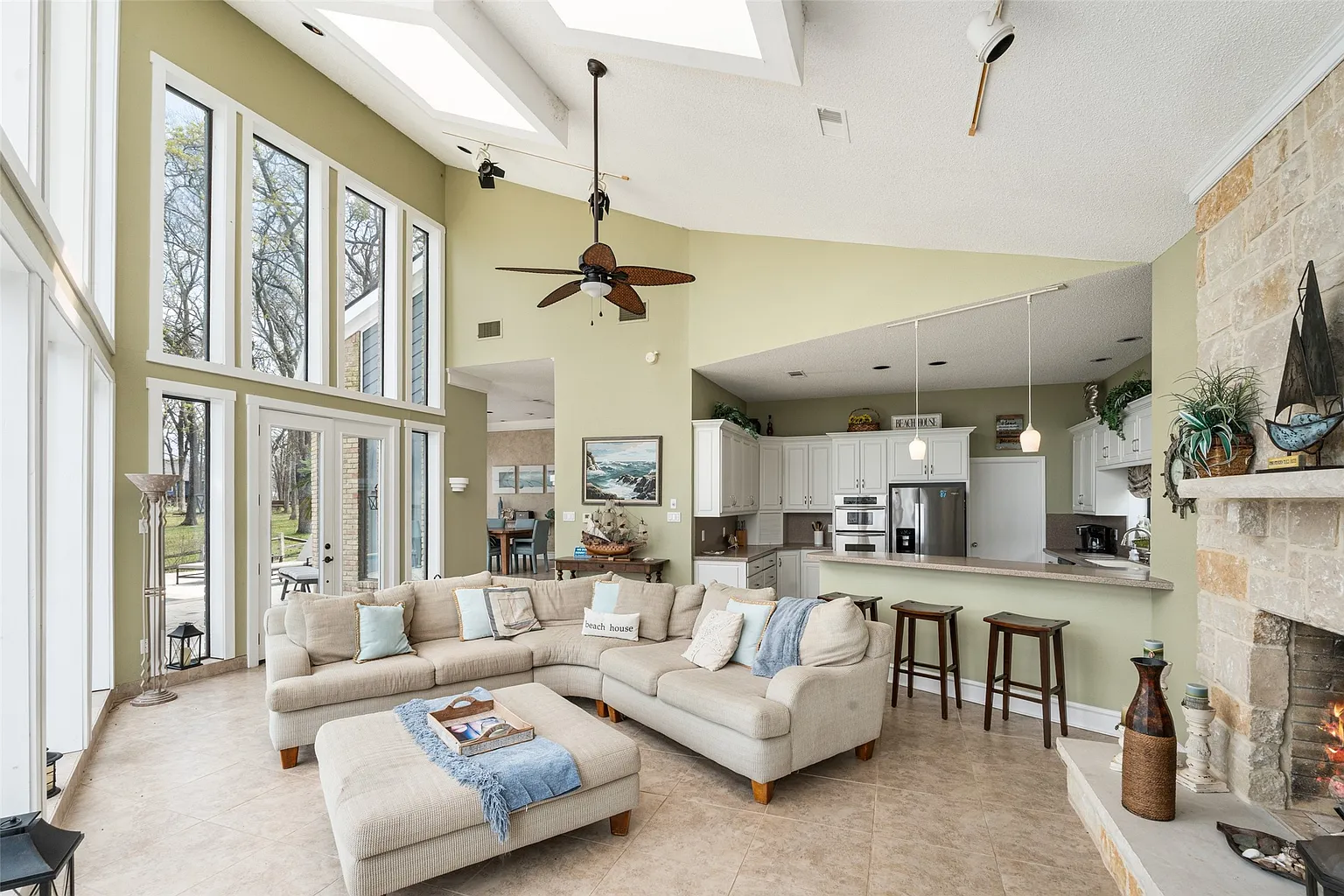 A large sectional curves through the center of the room, facing the lake and a TV mounted next to the stone fireplace.