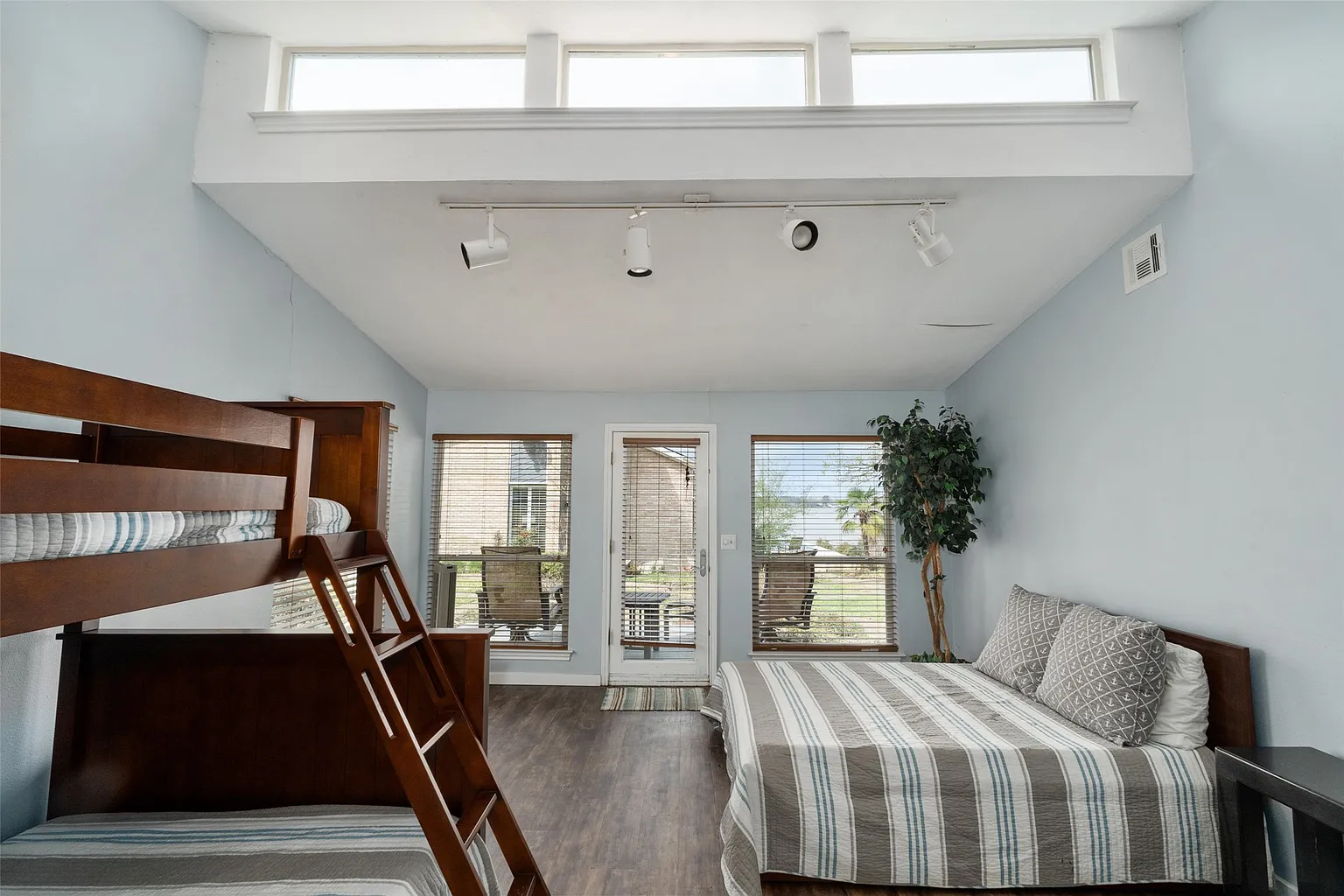 The bunk room, which combines a full bed with a stacked bunk along the opposite wall, leaving an open path through the center of the room to the deck outside.