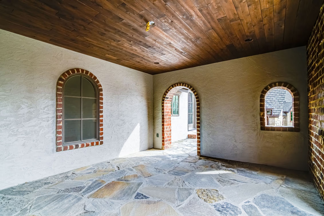 A front porch is finished with flagstone flooring, a dark wood-plank ceiling, and a mix of stucco and exposed brick.