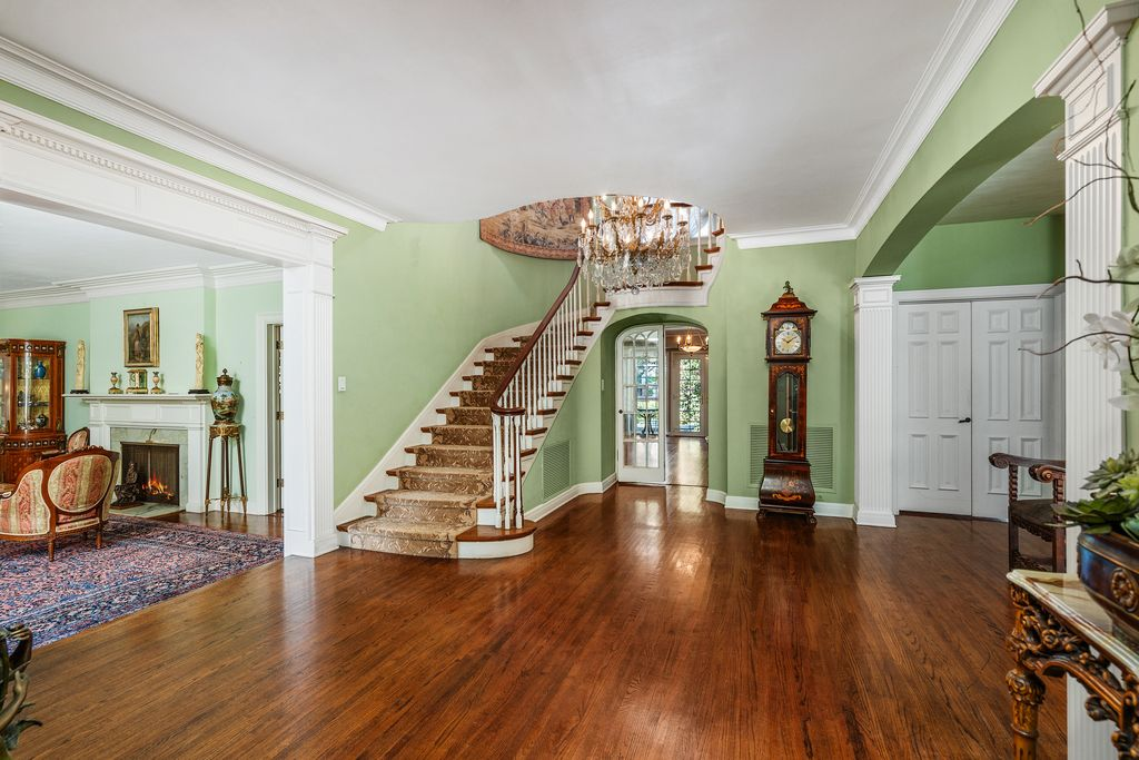 The home opens to a double-height foyer centered on a curved staircase that rises along the back wall beneath a crystal chandelier. 