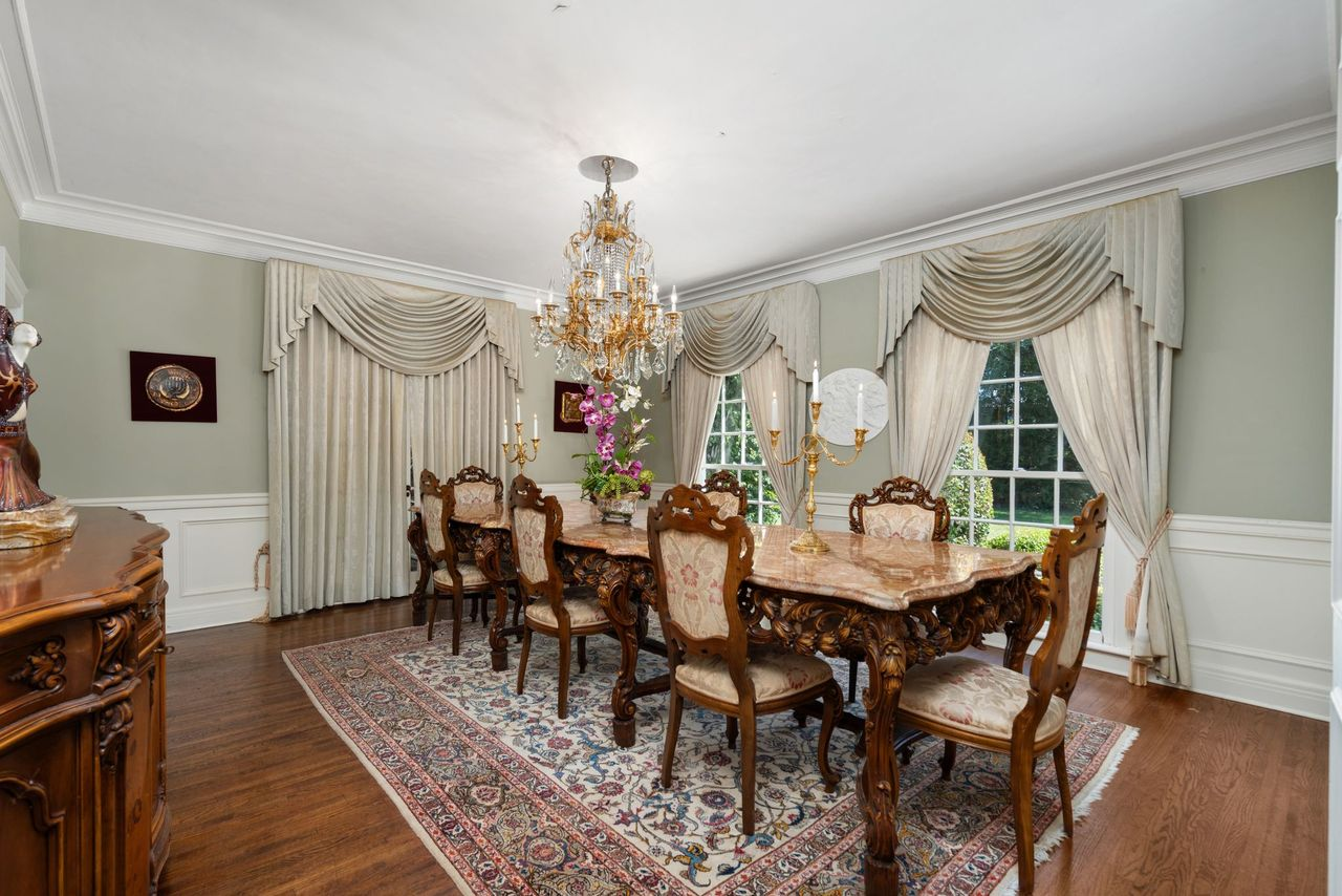 The formal dining room continues the home’s traditional interior with a long carved wood table set beneath a crystal chandelier.