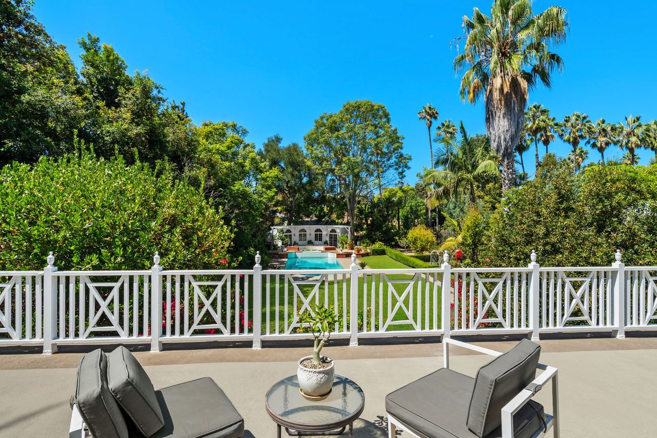 One of the rooms opens onto a private balcony overlooking the backyard, with a white railing framing views across the lawn and pool.