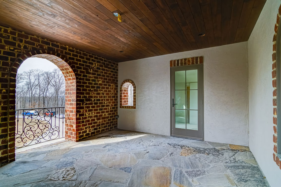 A series of arched openings frames views of the grounds, while brick-trimmed windows and wrought-iron railings lead toward a glass-paneled door.
