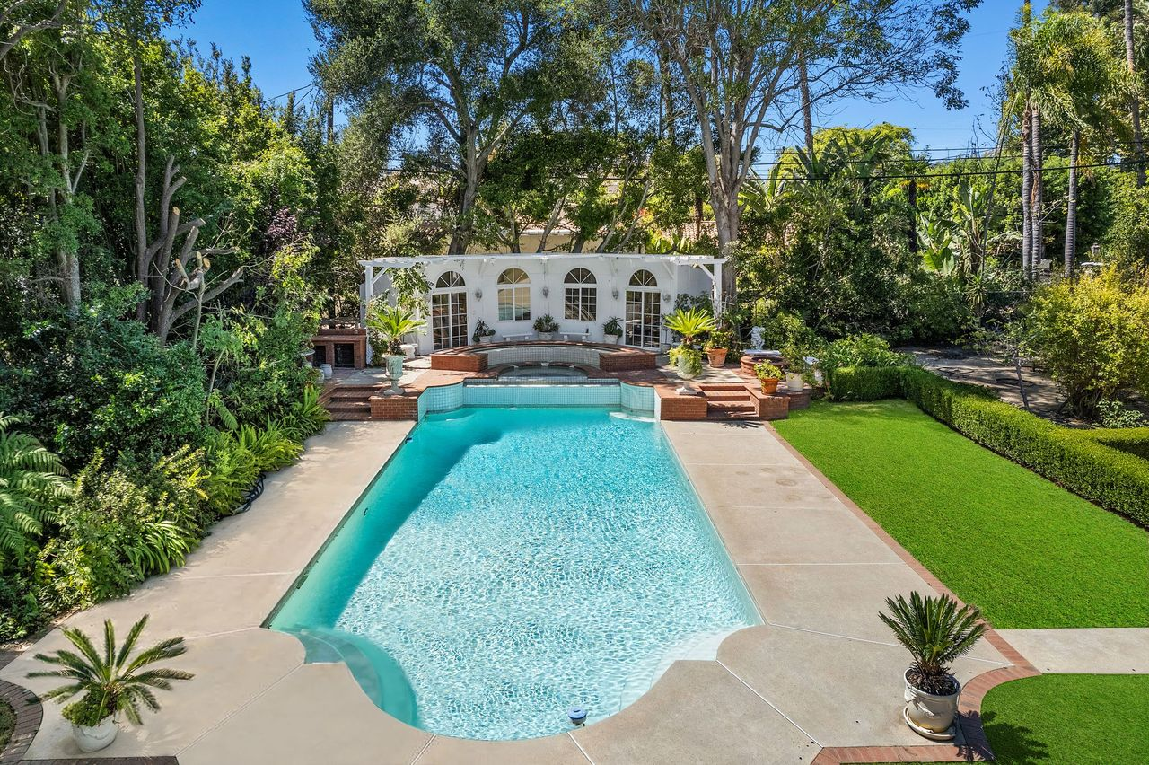 At the far end, a raised spa sits directly in front of the pool house pavilion, where a row of arched windows and doors faces back across the water and lawn.