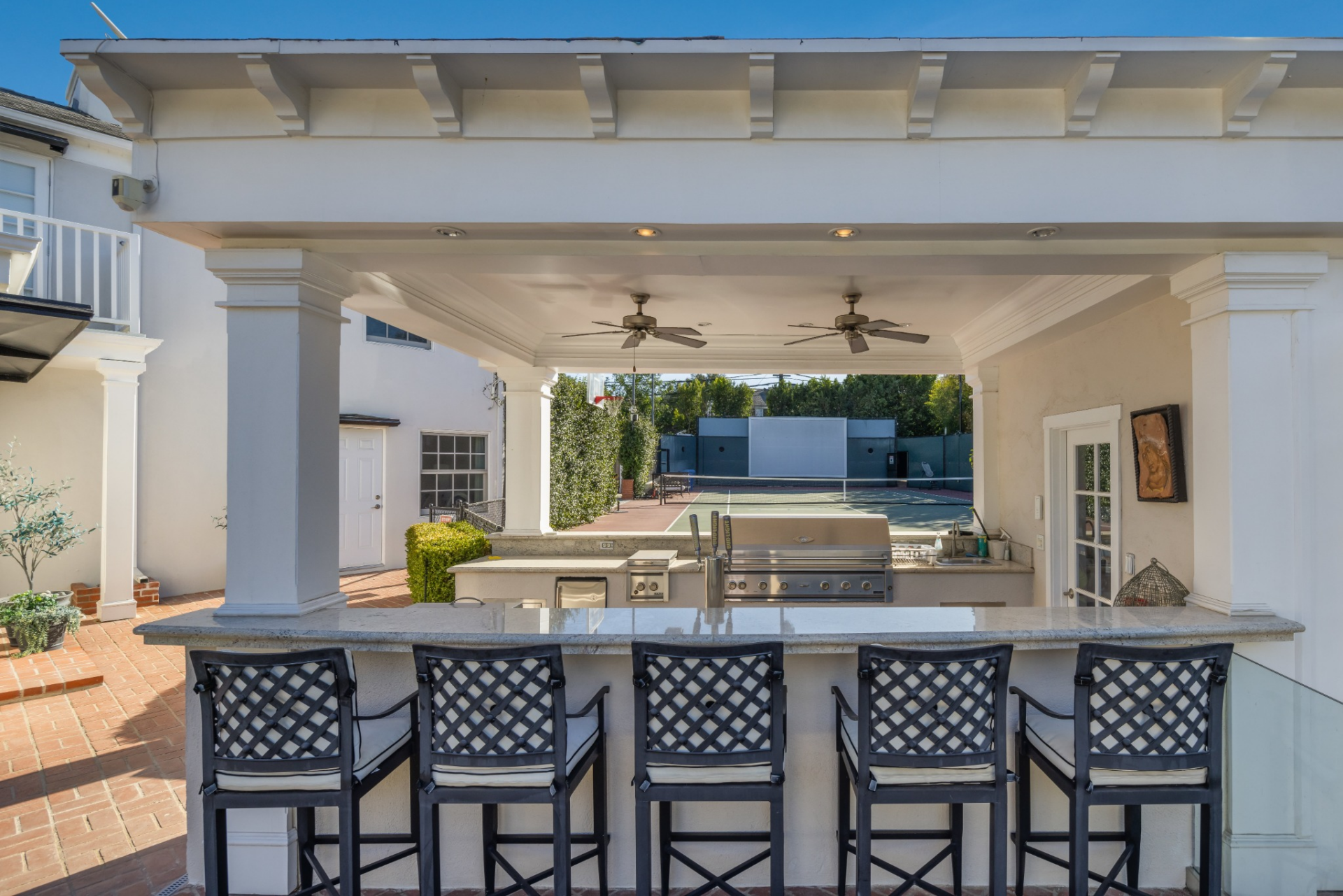 Covered outdoor kitchen with a long stone-topped bar and seating for five on one side and a built-in grill on the other.