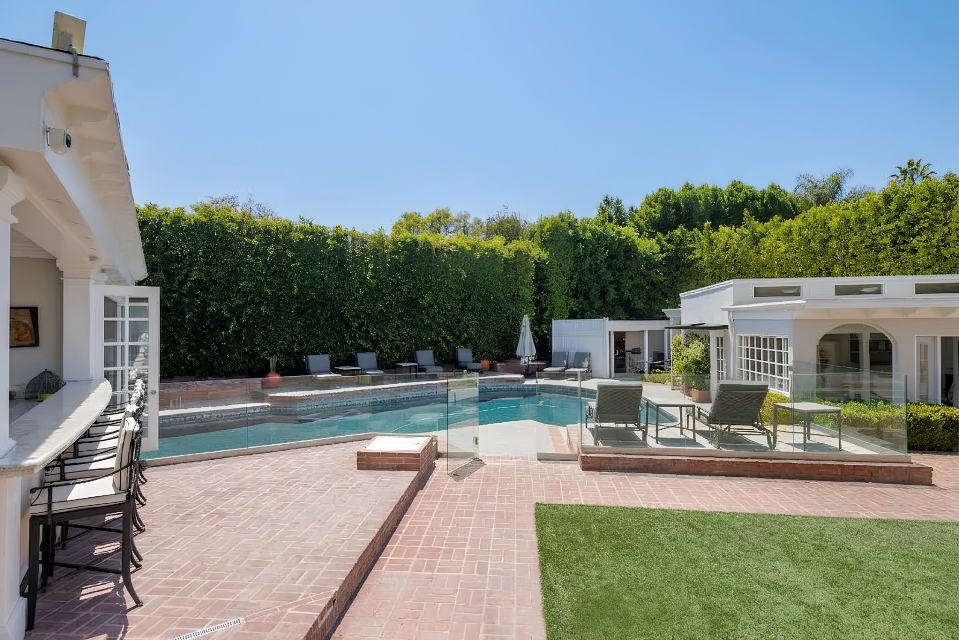 In the middle of the backyard, a glass gate opens to the pool, which is surrounded by multiple poolside lounge chairs.