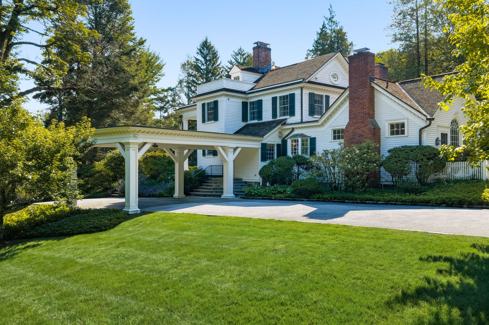 A long driveway winds through the trees before reaching a porte-cochère positioned along the side of the house.