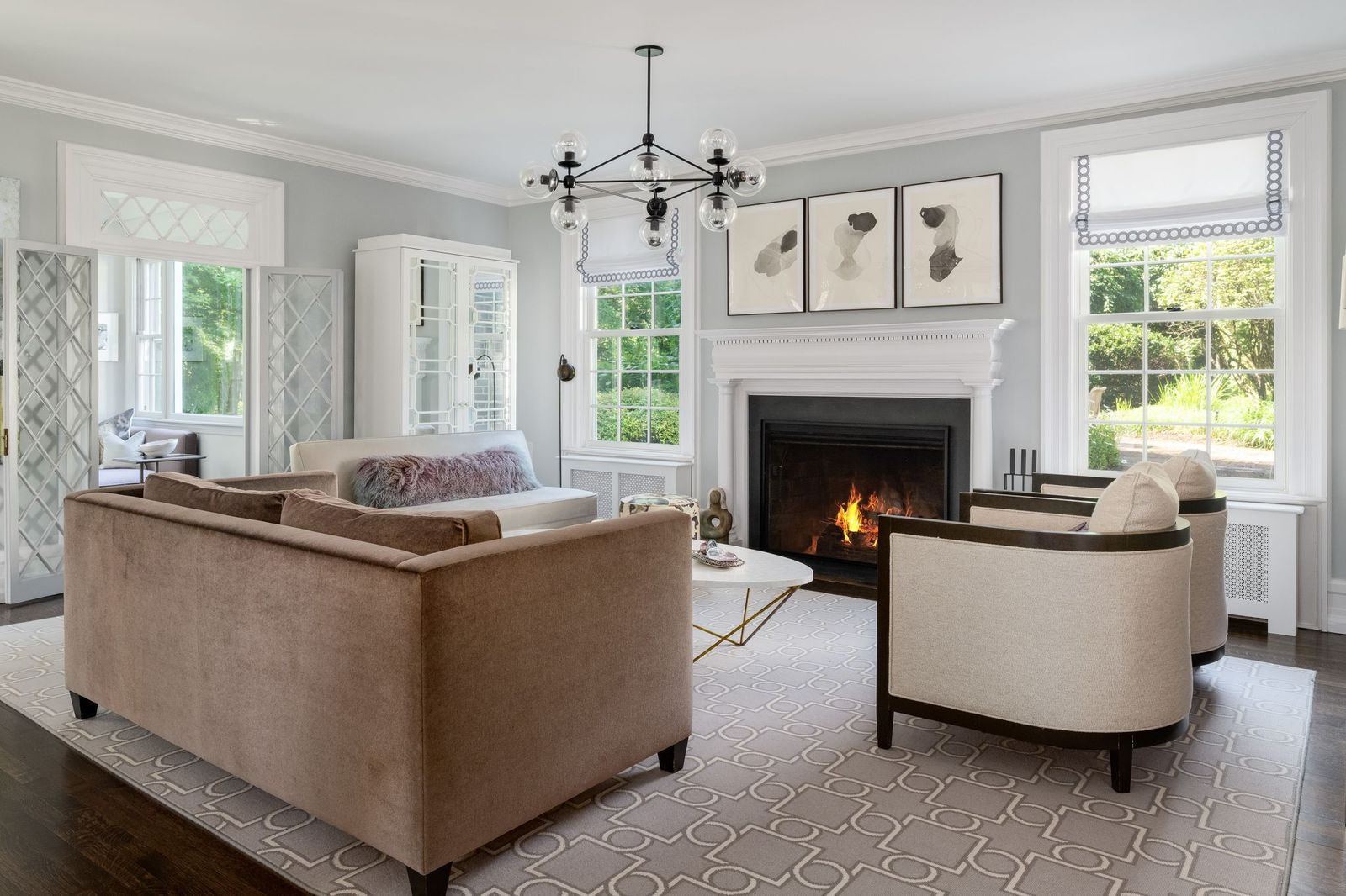 A pair of sofas and curved armchairs gather around the fire over a large patterned rug, while windows bring in views of the surrounding grounds.