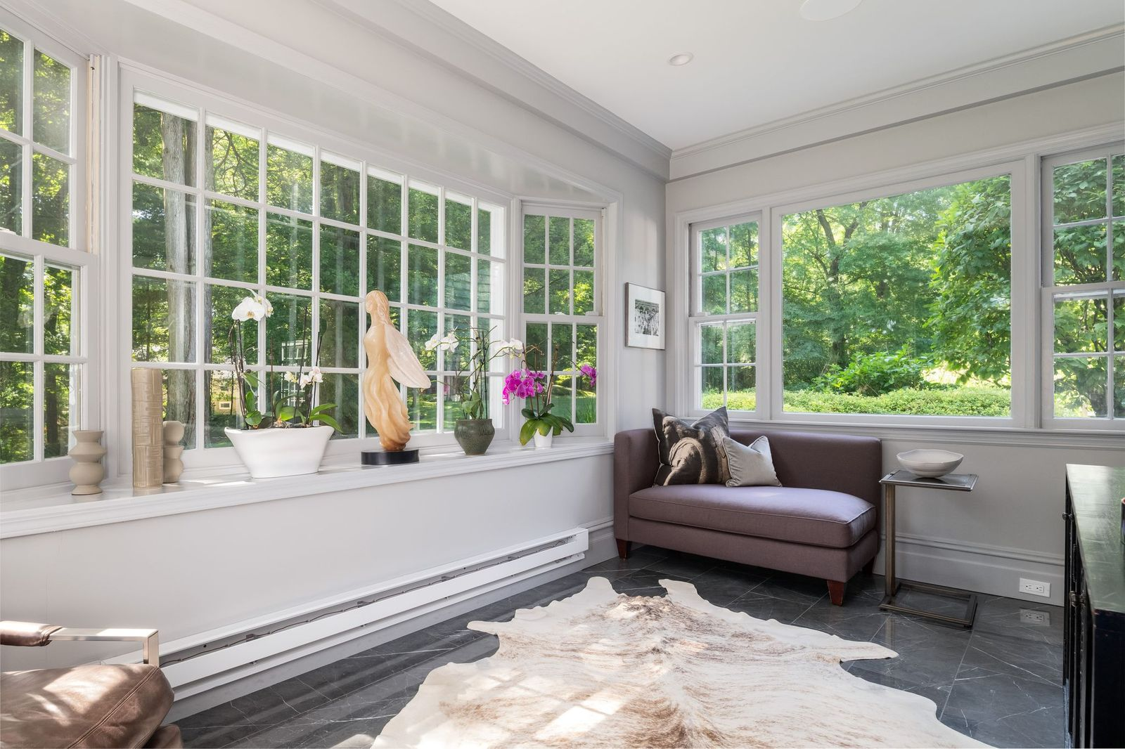 In the sunroom oversized multi-pane windows wrap the wall framing the lush woods and landscaped grounds that surround the house.