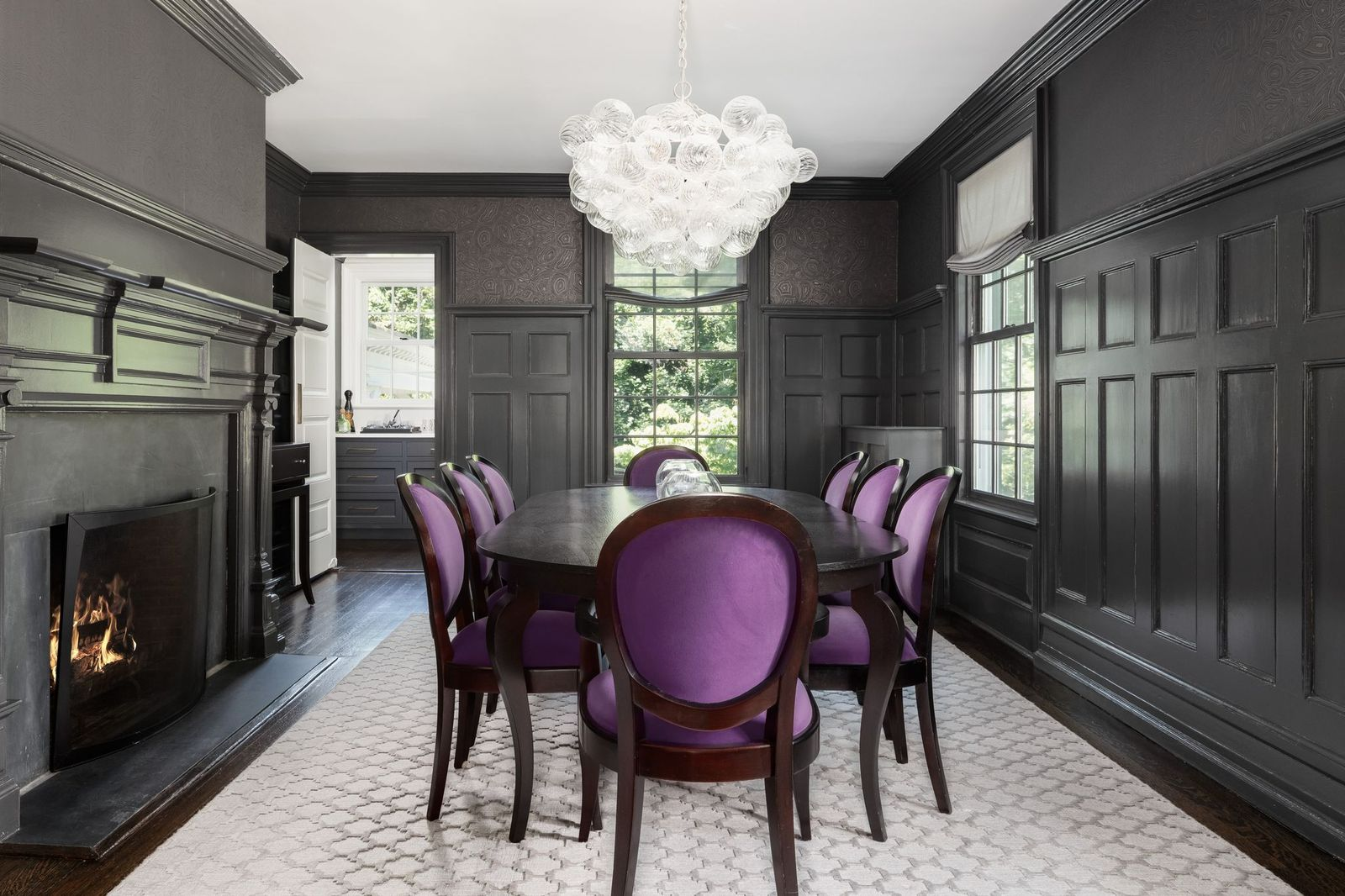 In the center of the room, a long oval table surrounded by purple velvet chairs sits beneath a glass chandelier beside another fireplace.